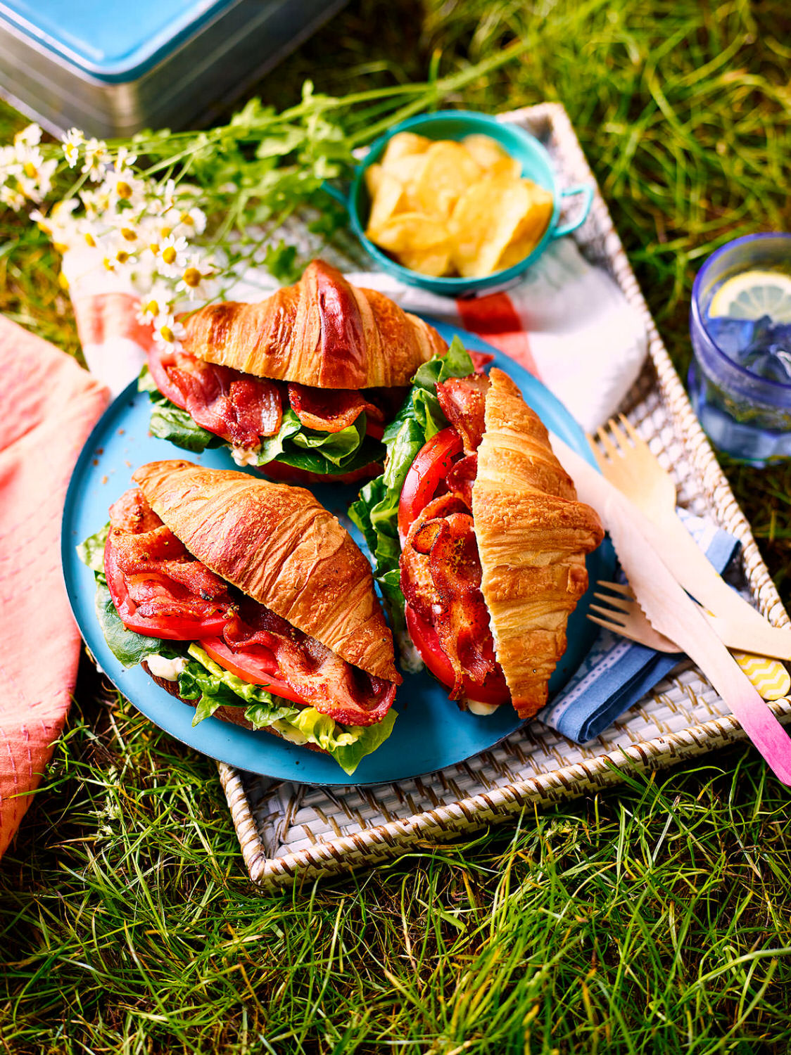 Croissants with bacon lettuce and tomato with mayo on a tray in an outdoor picnic setting