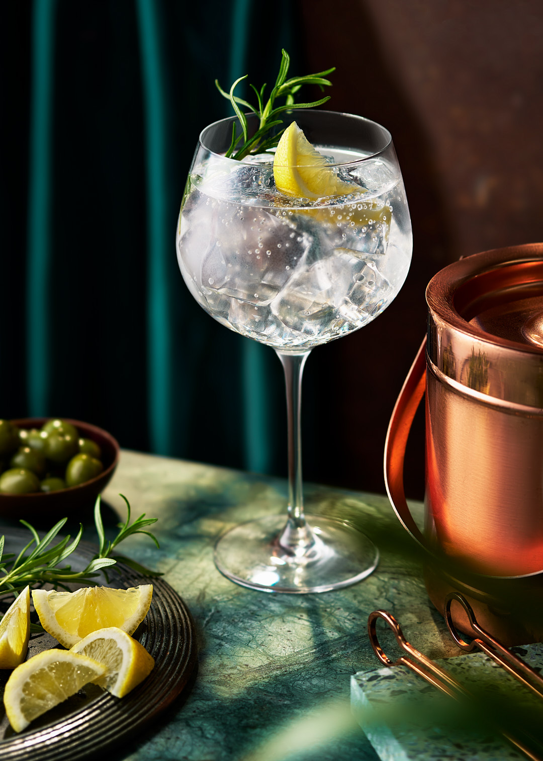 gin and tonic served in a large gin glass with rosemary and lemon. 