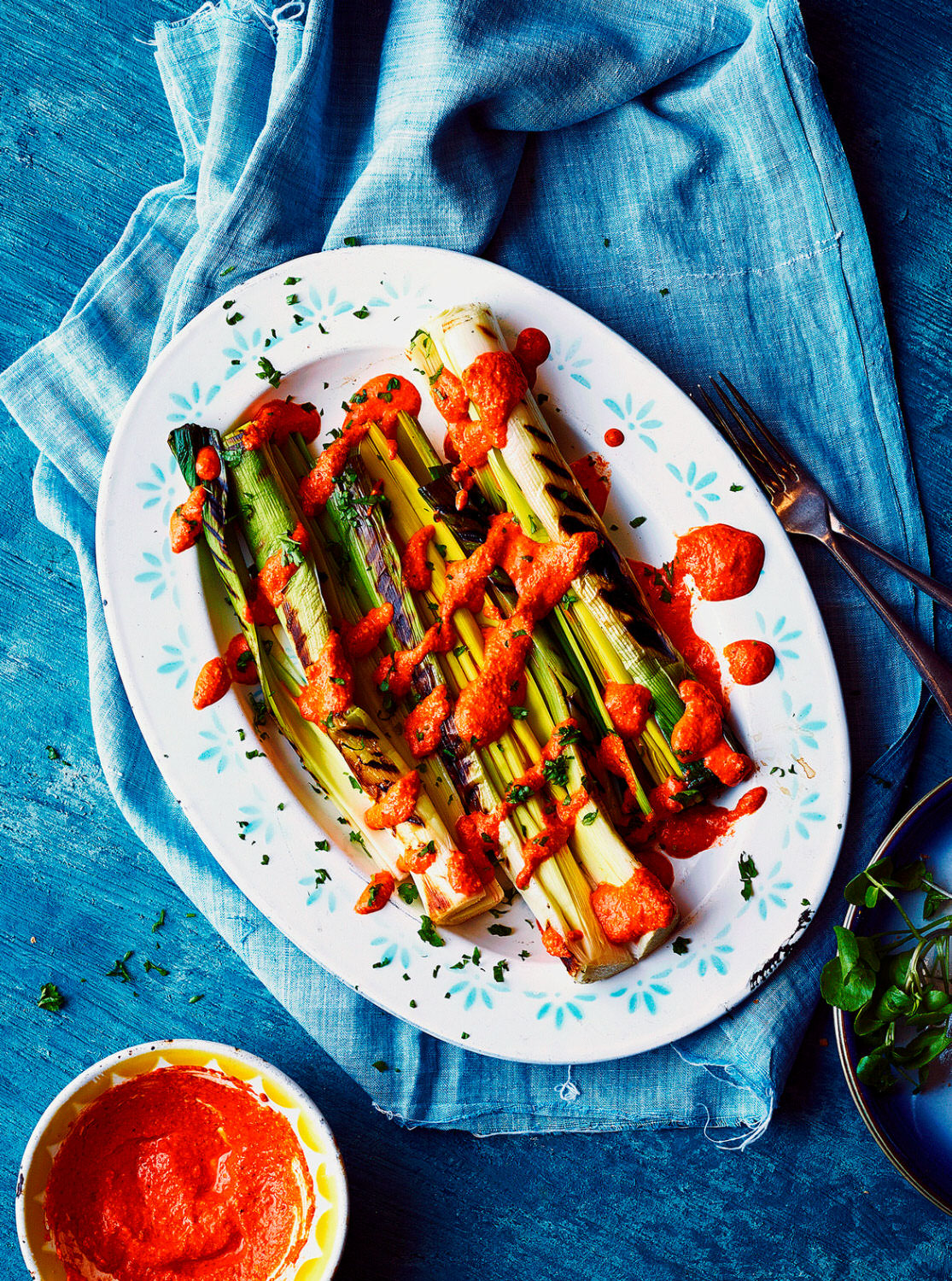 BBQ Leeks served on a white oval plate with a drizzling of  Walnut Romesco Sauce over the top