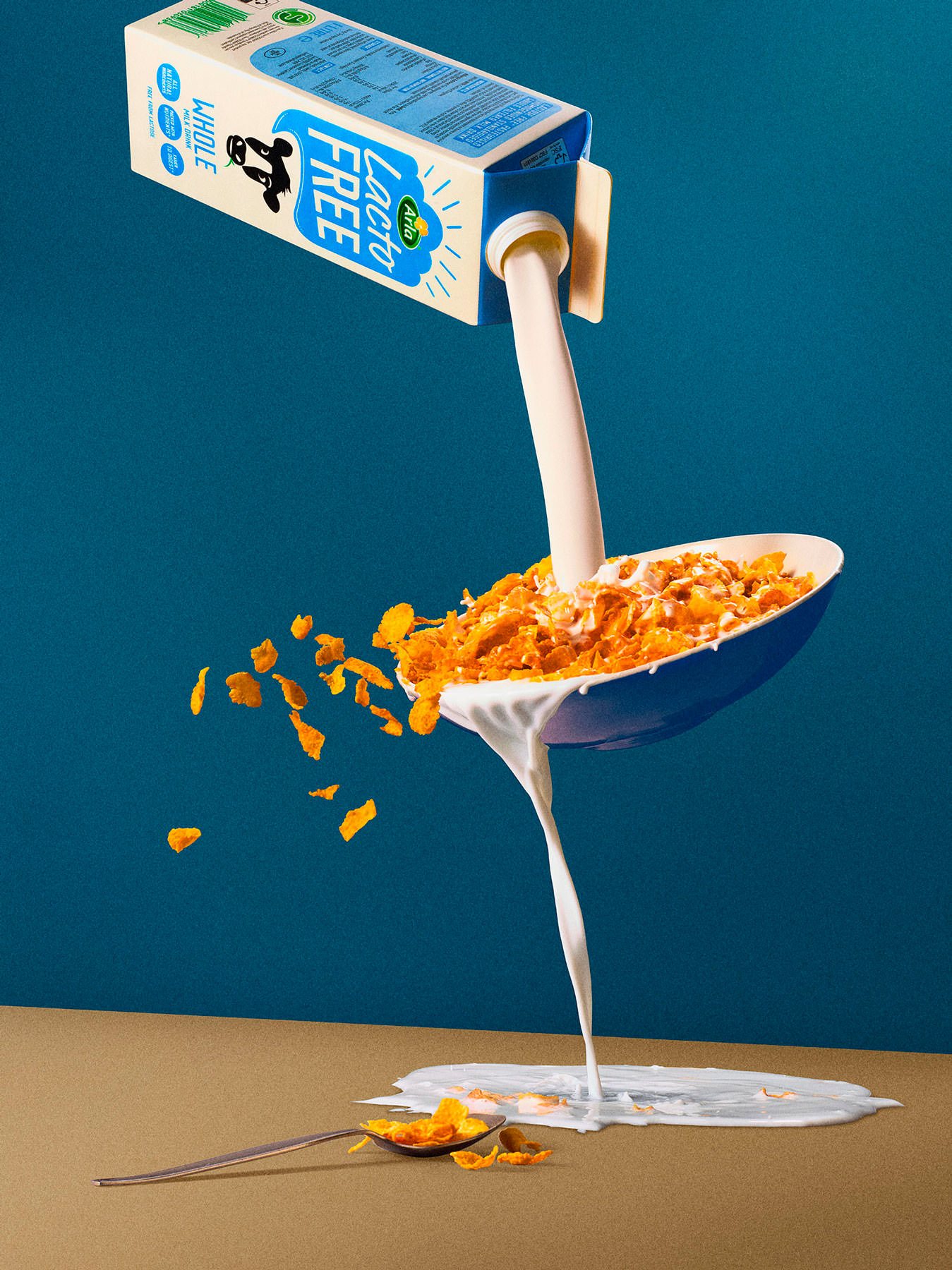 Carton of milk poring into a bowl of cornflakes which is over spilling in midair and cornflakes flying out of bowl - London Food & Drinks Photographer
