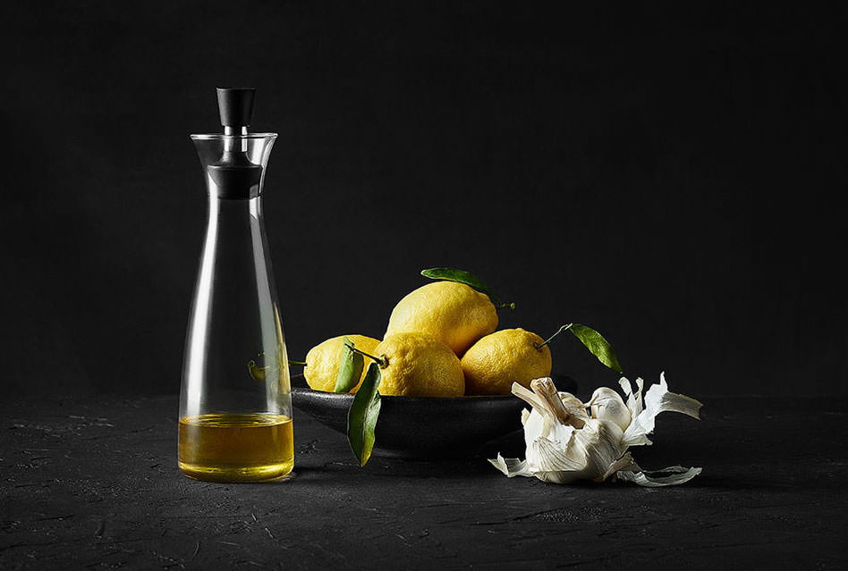 Olive oil in a contemporary bottle next to a bowl of fresh lemons and peeled garlic bulb - London Food & Drinks Photographer