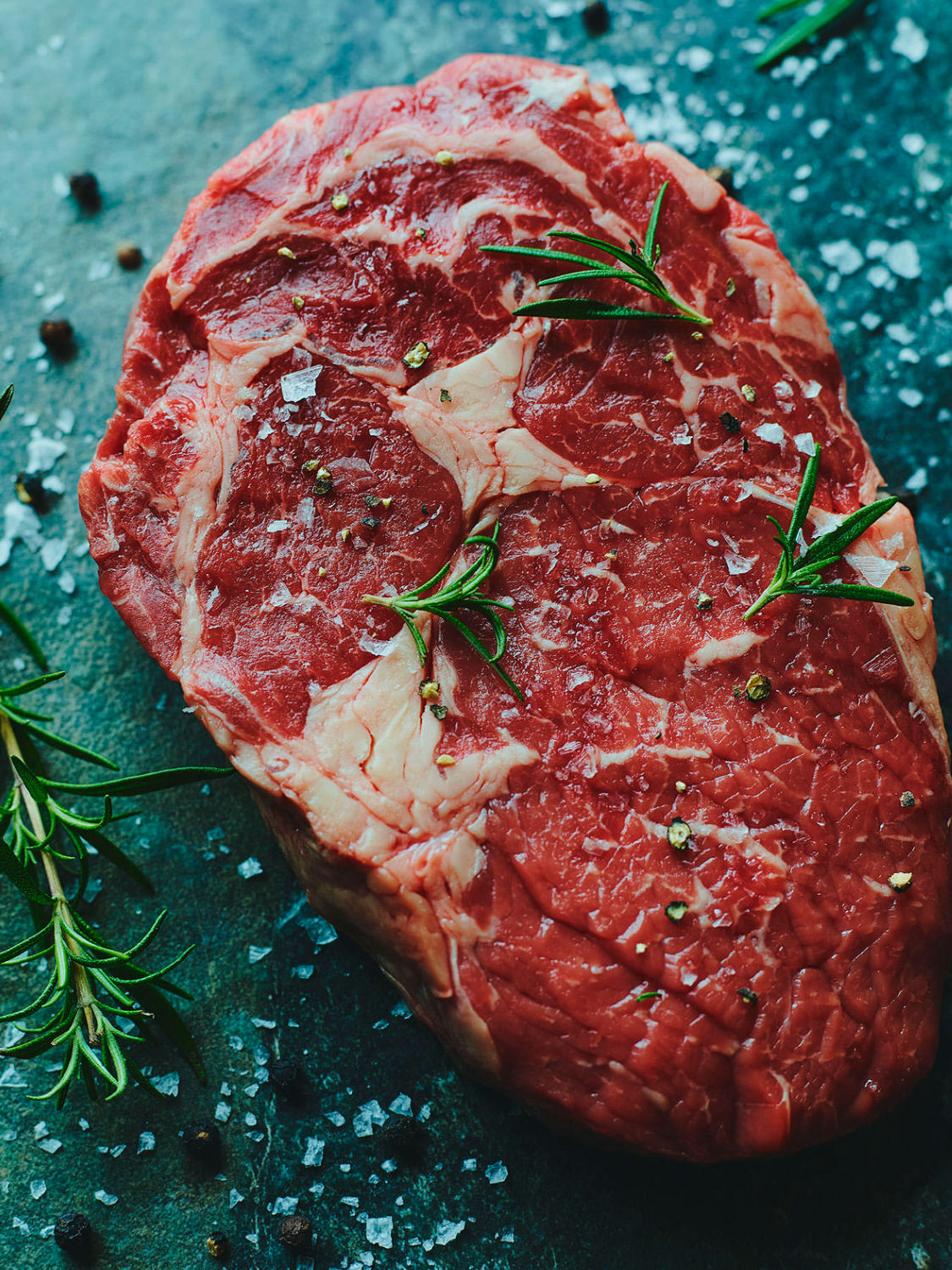 Close up of a fresh cut of rib eye steak seasoned with fresh herbs and salt and pepper. 