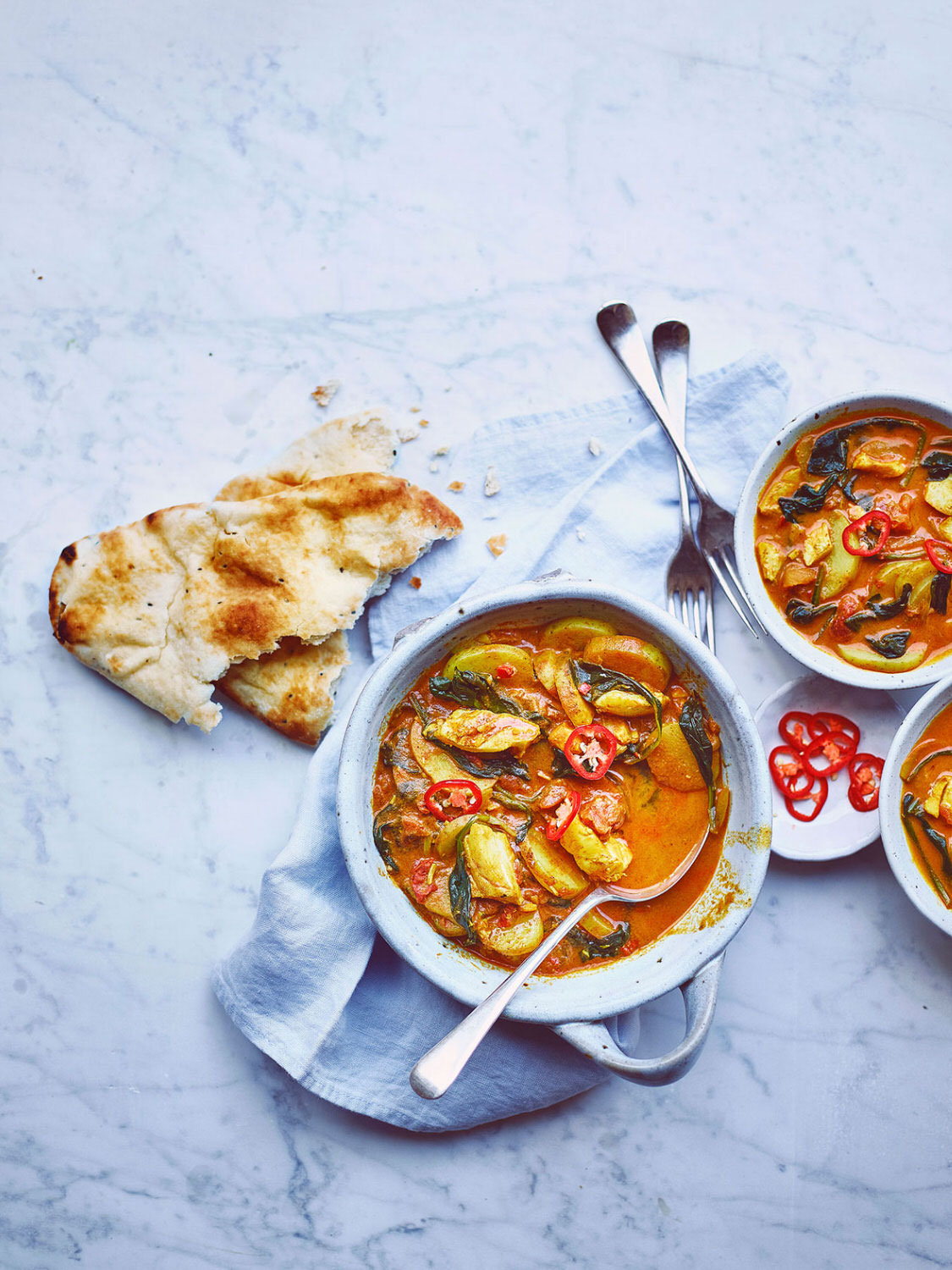 Fish curry served in ceramic curry bowls with naan breads