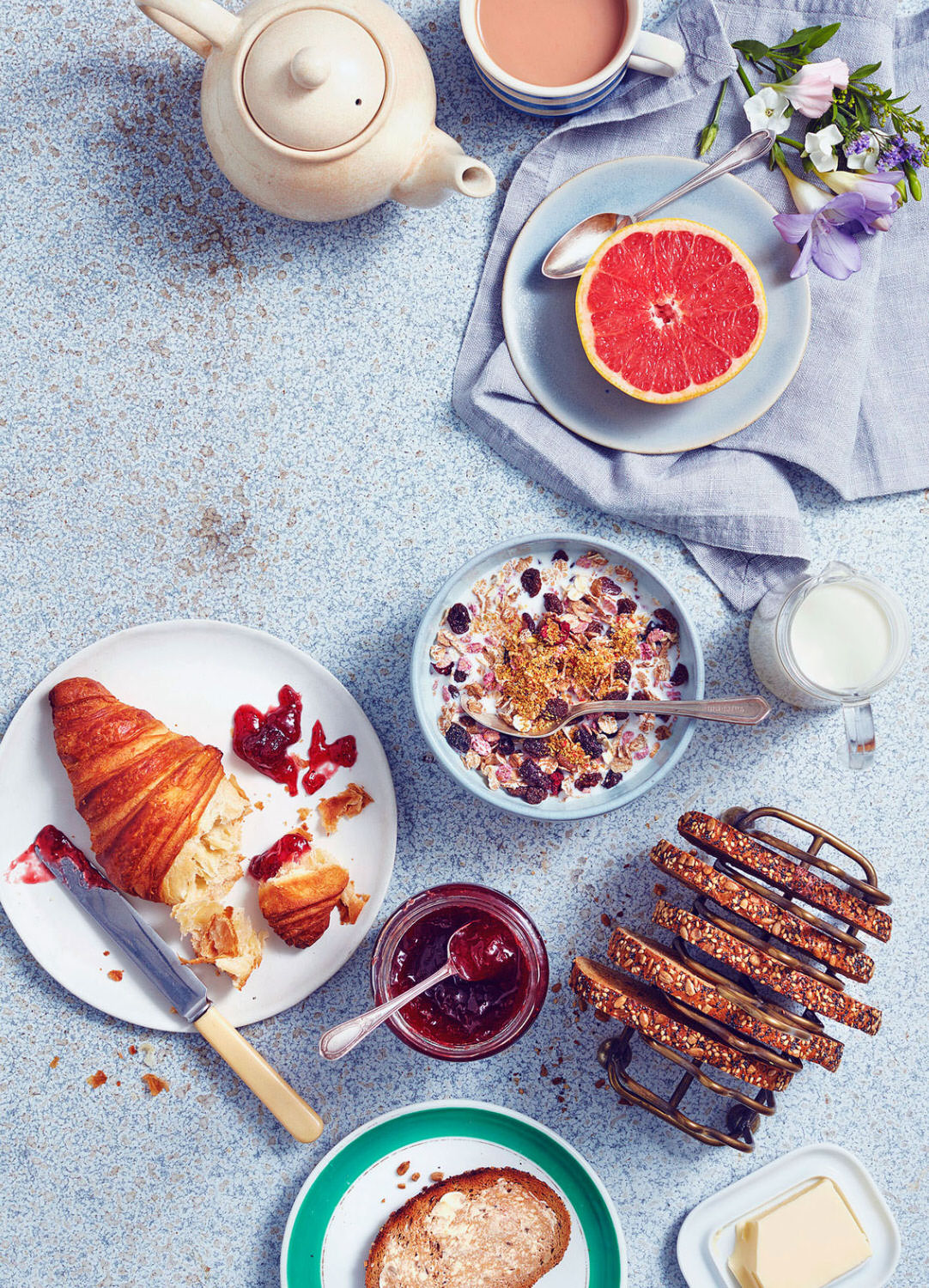 Breakfast spread consisting of croissants with jam, granary toast, tea, granola and  grapefruit