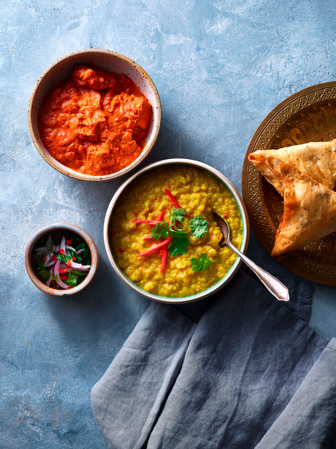 Tarka Dhal in a bowl served with samosas and curries